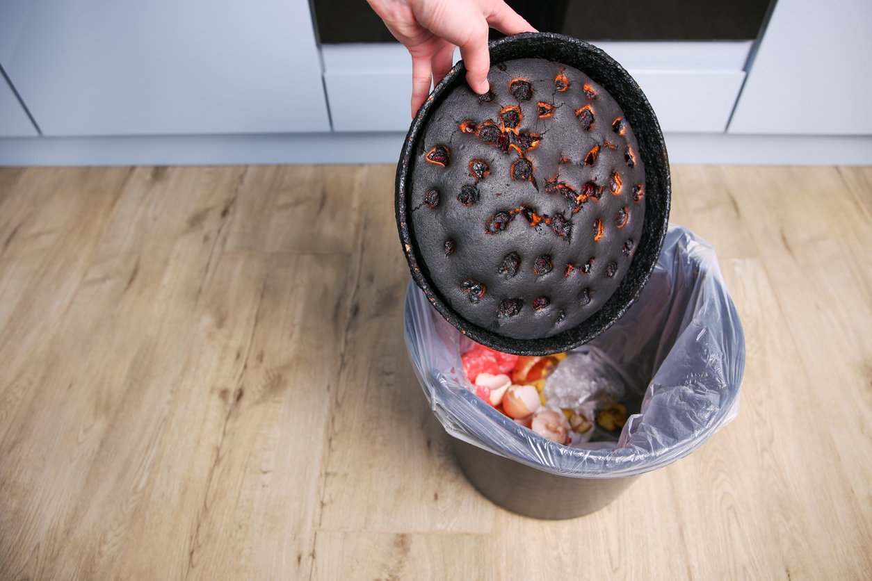 A woman throws a burnt pie in the trash.