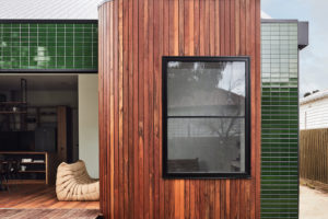 Malý ekologický moderní domeček geometrických tvarů se zeleným a hnědým obkladem