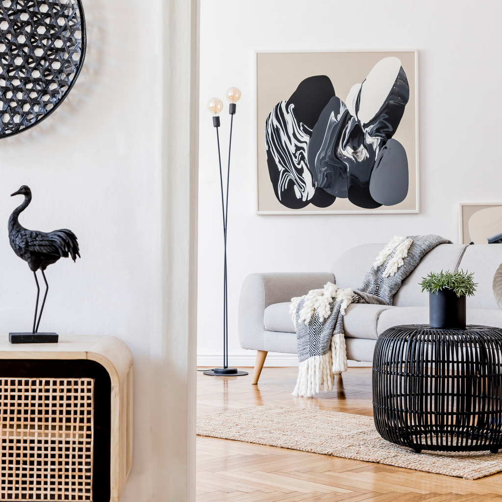 Moderní skandinávský design interiéru otevřeného prostoru se stylovou dřevěnou komodou, šedou pohovkou, ratanovým stolem, rostlinou, tropickým listem a elegantními doplňky