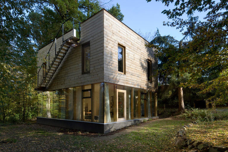 Dřevěný dům s mnoha úrovněmi soukromí: otevřené přízemí s prosklenými fasádami a skrytá střešní terasa