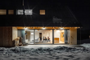 Pohled do prosklenné kuchyně, kde sedí rodina - Moderní dřevostavba