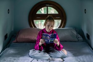 Mladá dívka sedí na posteli s knihou -Letadlový dům