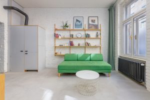 Obývací pokoj se zeleným gaučem a nad ním polička