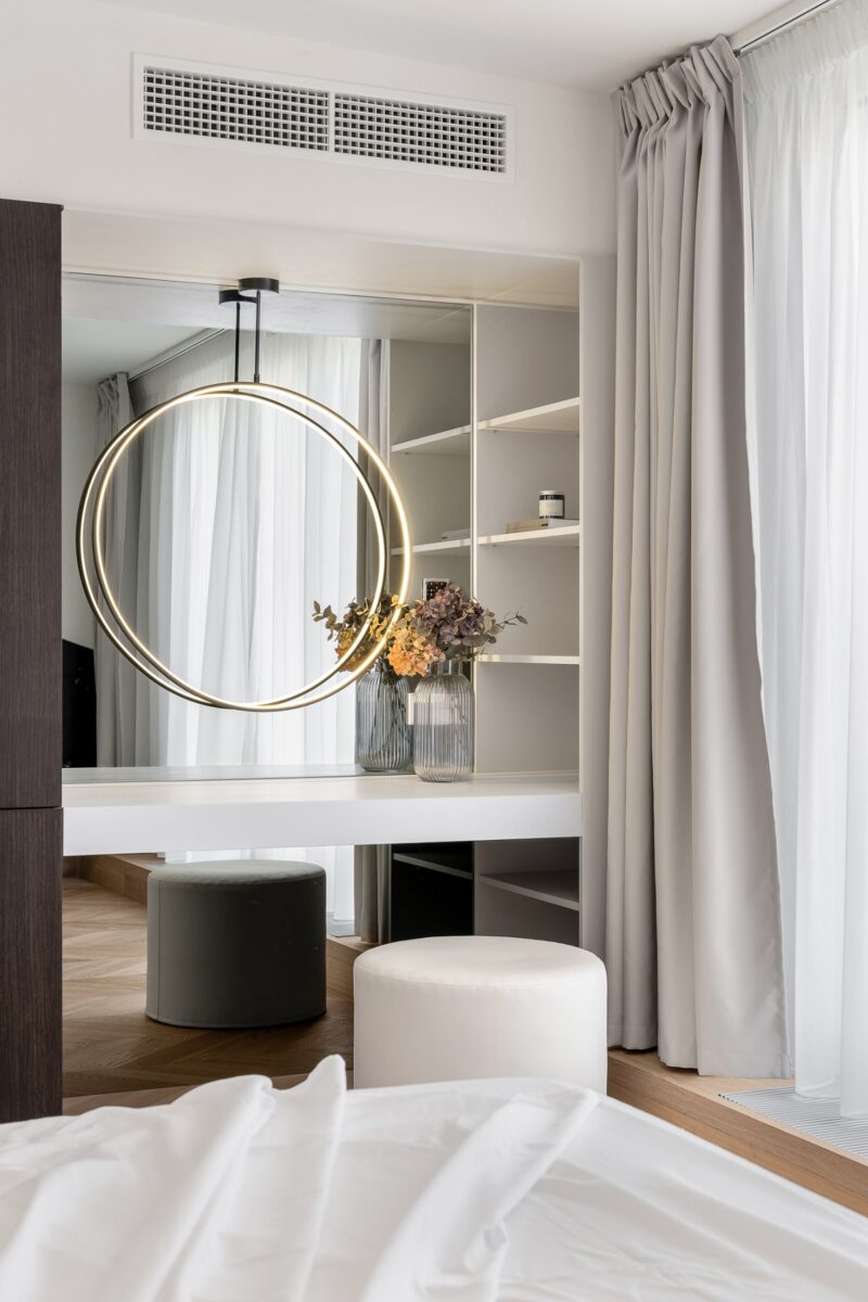 Ložnice s moderním nádechem, kde dominuje velké kulaté zrcadlo.