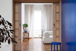 Chodba s dřevěnou podlahou, modrými skříňkami a výhledem do světlého obývacího pokoje.