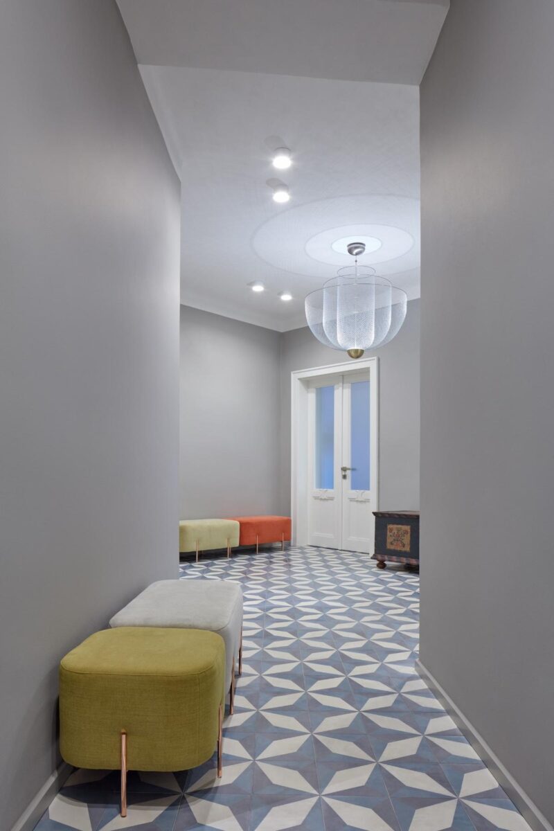 Barevné lavičky poskytují praktické místo k sezení, zatímco geometrické dlaždice na podlaze přidávají prostoru dynamiku a vizuální zajímavost.