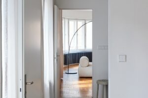 Pohled do obývacího pokoje s bílou pohovkou a velkým obloukovým světlem, viděný z chodby.