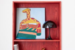 Červený výklenek s obrázkem žirafy, malou černou lampičkou a knihami.
