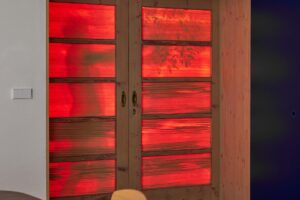 Dřevěné dveře s matným sklem, osvětlené červeným světlem, vytvářejí dramatický efekt v moderním interiéru.
