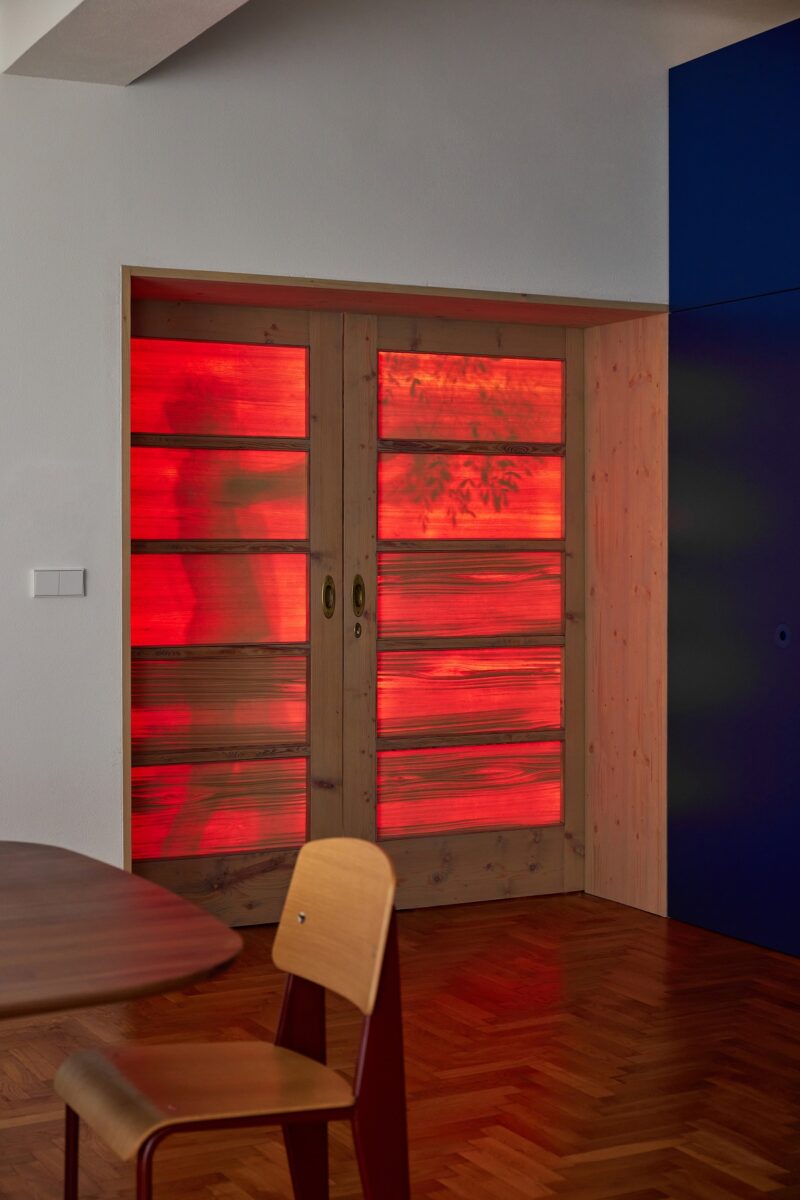 Dřevěné dveře s matným sklem, osvětlené červeným světlem, vytvářejí dramatický efekt v moderním interiéru.