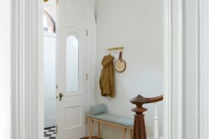 Bílé vstupní dveře a dřevěná lavice vytvářejí elegantní a příjemný vstupní prostor.