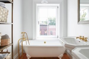 Elegantní koupelna s volně stojící vanou, zlatými kohoutky a dřevěnou podlahou.