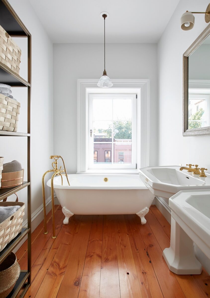 Elegantní koupelna s volně stojící vanou, zlatými kohoutky a dřevěnou podlahou.