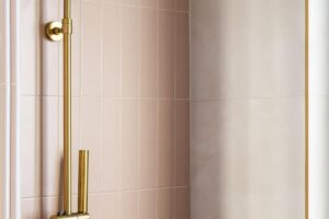 Sprchový kout s růžovými dlaždicemi a zlatou sprchovou hlavicí.