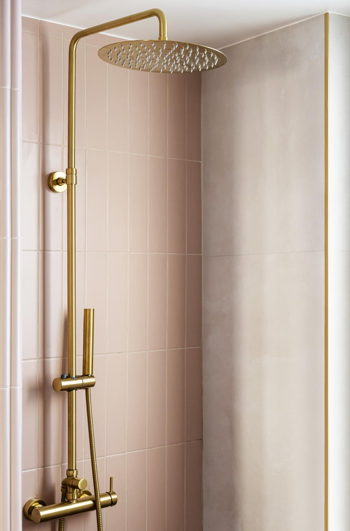 Sprchový kout s růžovými dlaždicemi a zlatou sprchovou hlavicí.
