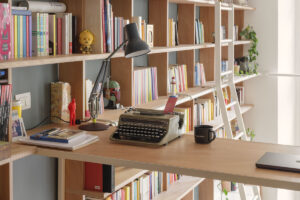 Detail pracovního kouta s dřevěným stolem, retro psacím strojem a knihovnou na míru přes celou stěnu