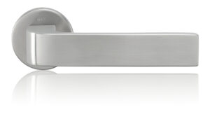 Detailní pohled na moderní dveřní kliku z matné nerezové oceli s minimalistickým designem a jemným odleskem, na bílém neutrálním pozadí.