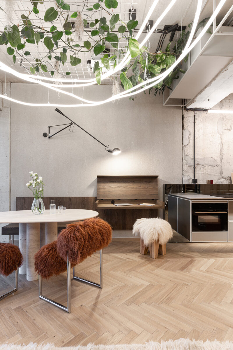 Detail jídelního koutu s oválným stolem, designovými židlemi s chlupatým potahem a zavěšeným stropním osvětlením propleteným zelení.