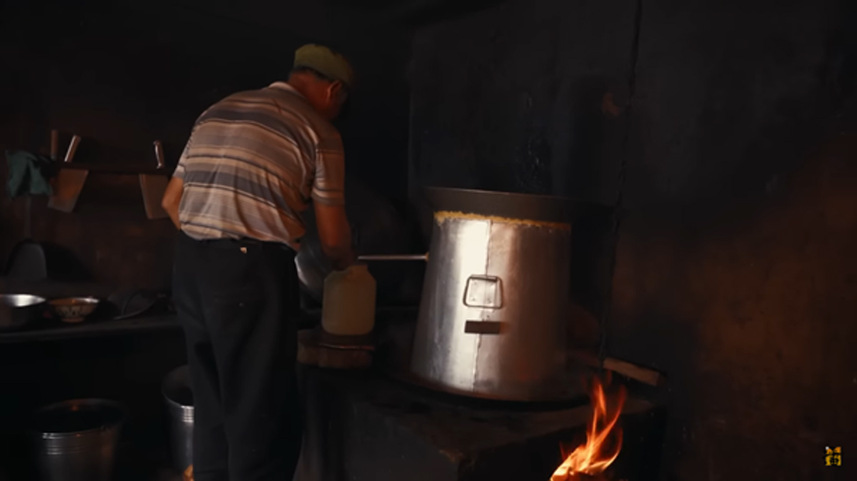Starší muž připravuje pálenku v tradiční palírně s kotlem na dřevo.