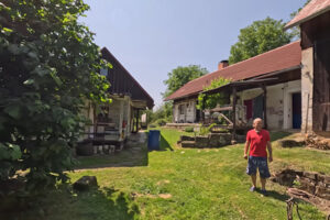 Dvůr s chalupou a hospodářskými budovami, muž stojí na trávníku