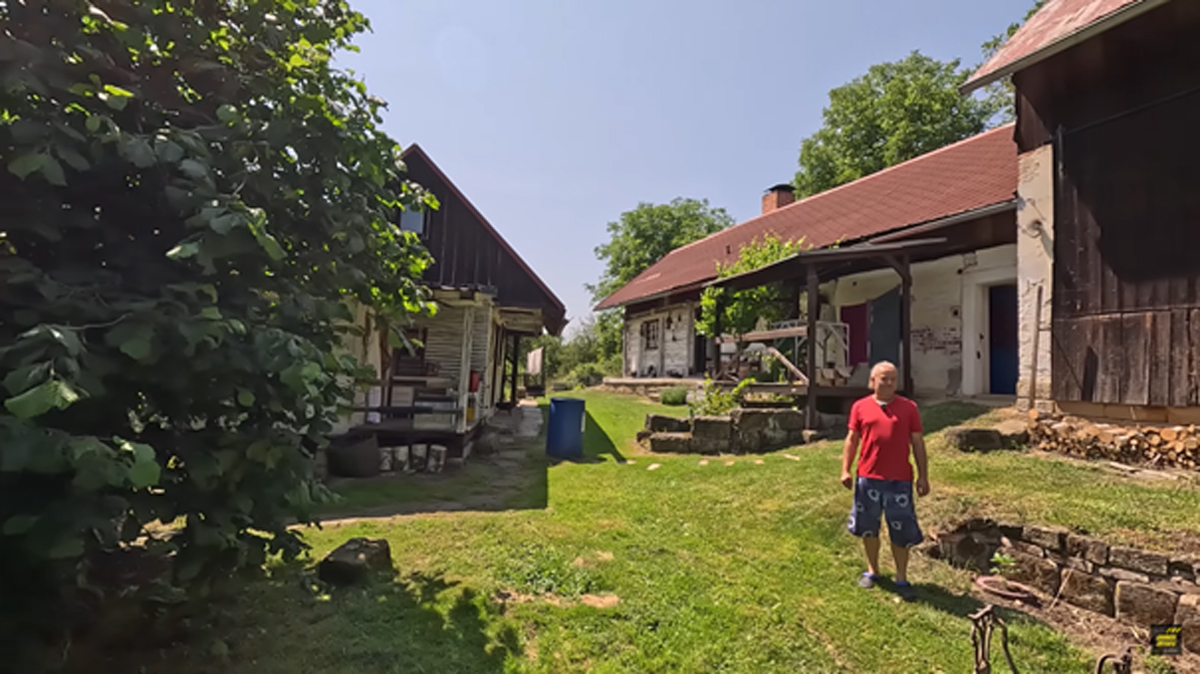 Dvůr s chalupou a hospodářskými budovami, muž stojí na trávníku