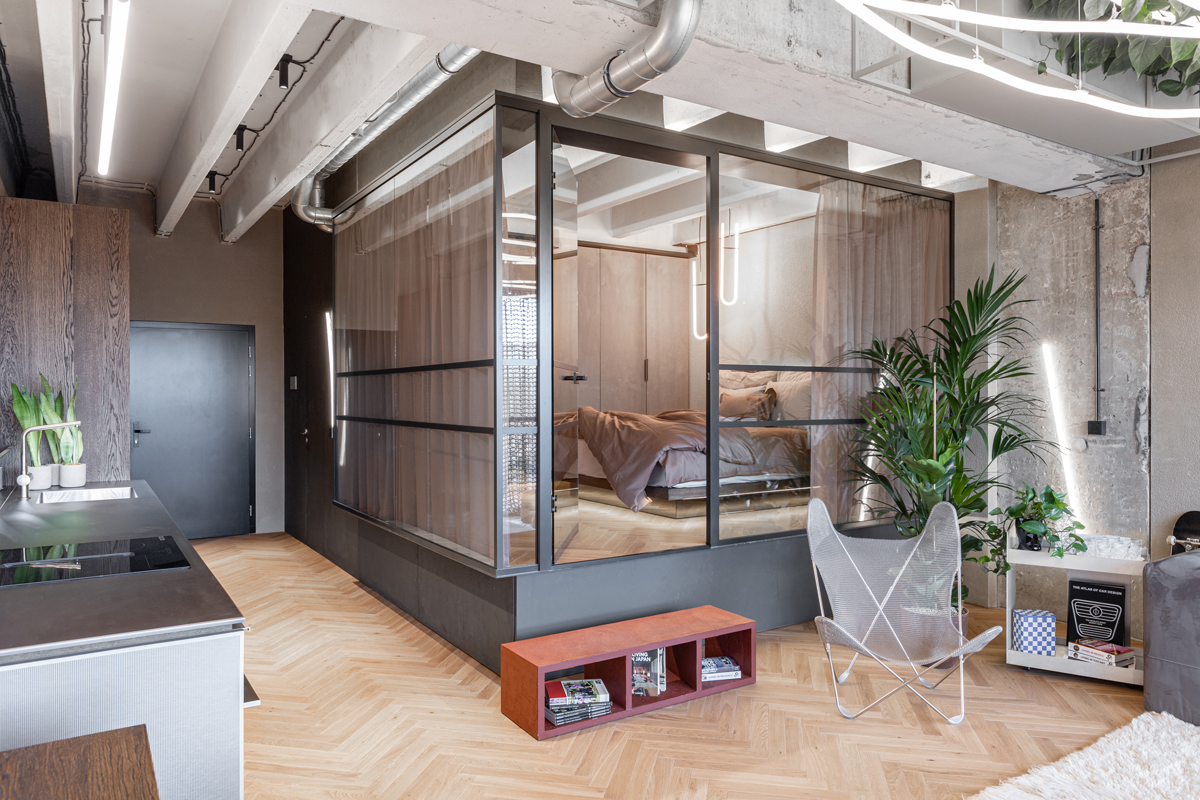Designová ložnice oddělená prosklenou stěnou se zataženými závěsy, minimalistickou postelí s měkkým povlečením a jemným LED osvětlením vytváří útulný a přitom moderní pocit soukromí.