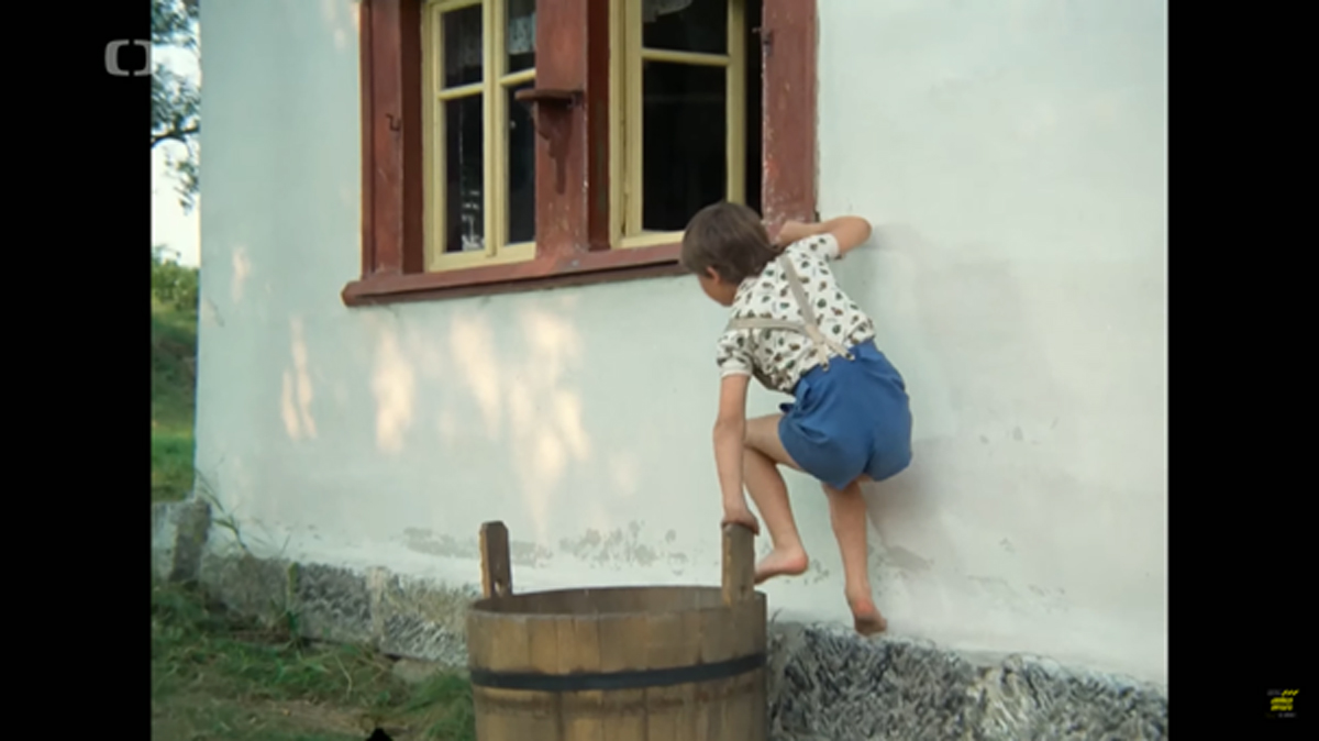 Filmová scéna: Chlapec v modrých kraťasech leze do chalupy oknem přes lavor