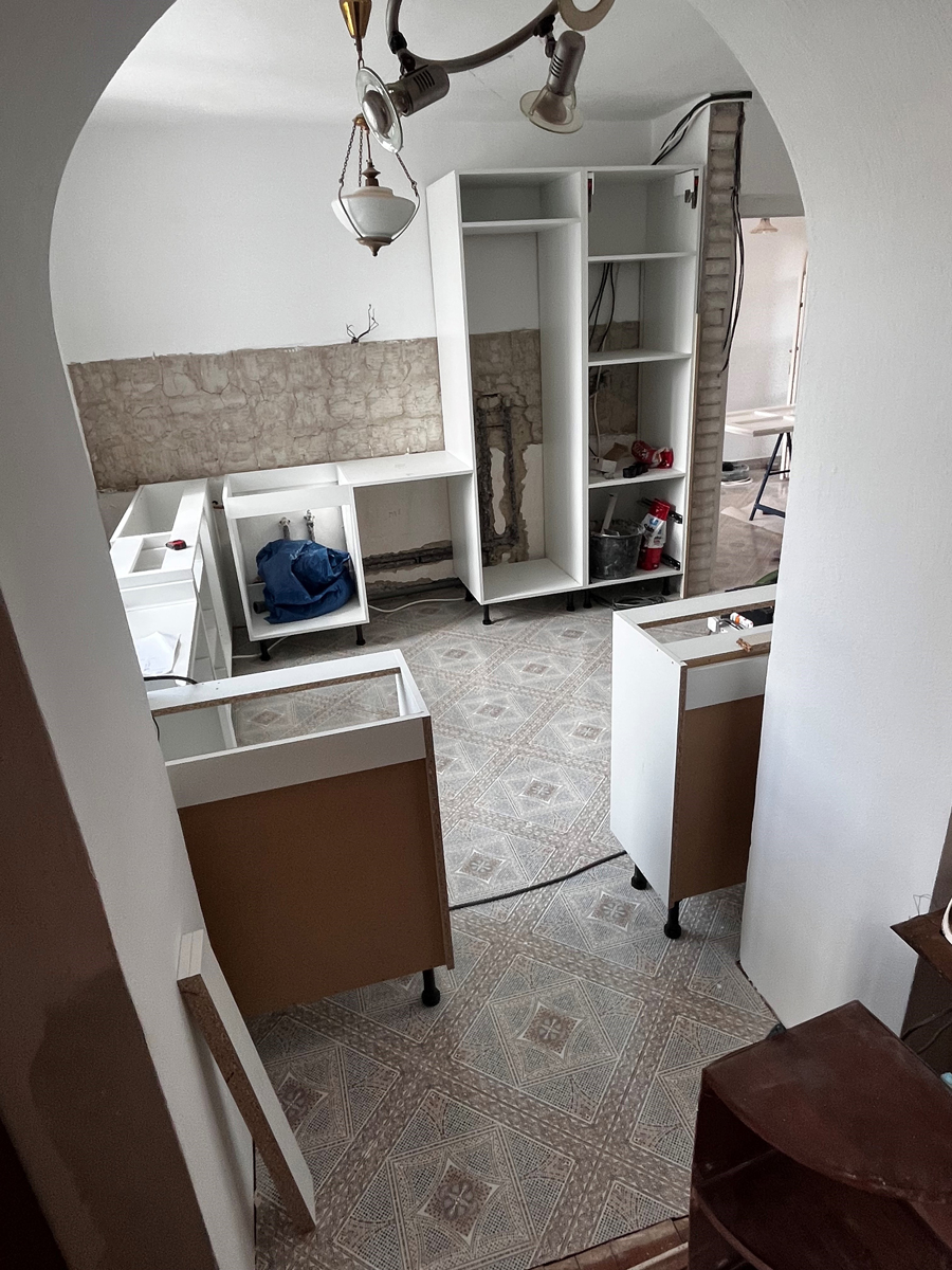 Montáž nové kuchyně – částečně smontované skříňky, odkryté zdivo a elektroinstalace.
