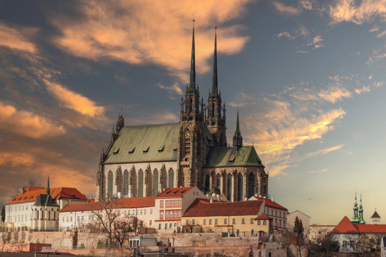 Panorama katedrály svatého Petra a Pavla v Brně při západu slunce s oranžově zbarvenou oblohou v pozadí.