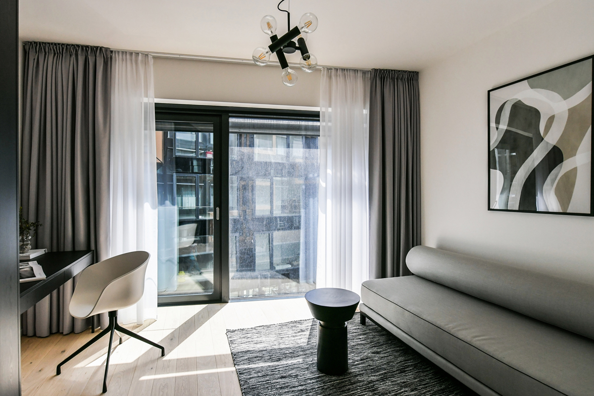 Moderní obývací pokoj s elegantním napínaným stropem a velkými okny – inspirace pro moderní interiéry s možností skrytého stropního vytápění.
