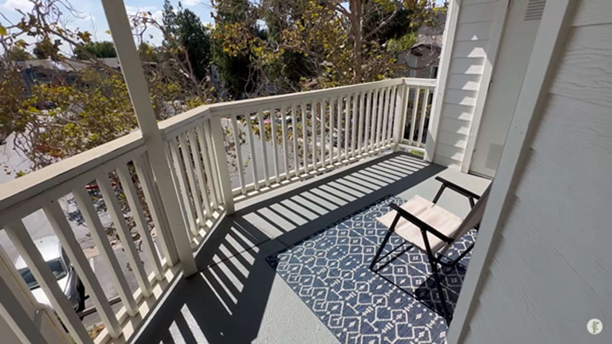 Prázdný balkon s jedinou židlí a kobercem s jemným vzorem.