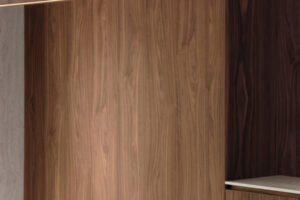 Designové svítidlo z masivního dřeva zavěšené nad jídelním stolem, v pozadí dřevěný obklad stěny.