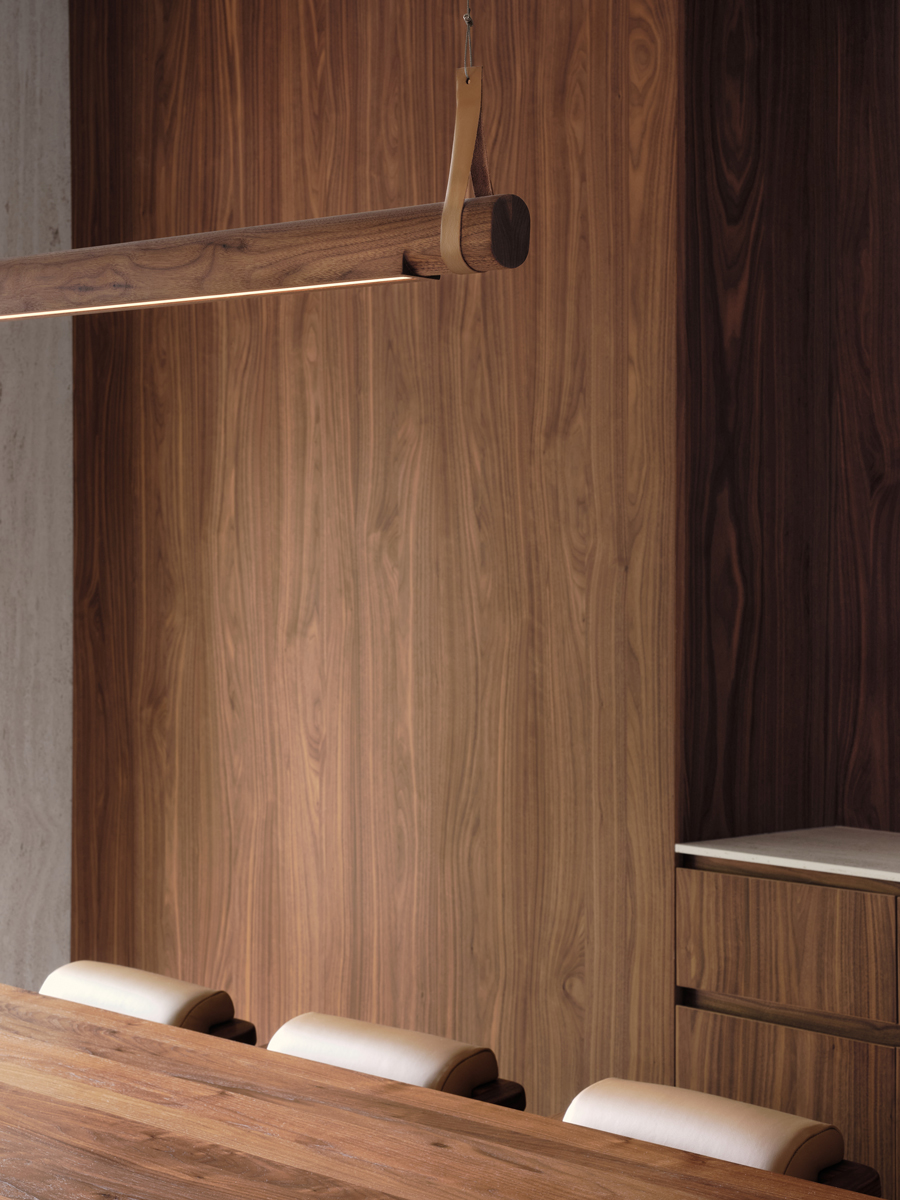 Designové svítidlo z masivního dřeva zavěšené nad jídelním stolem, v pozadí dřevěný obklad stěny.