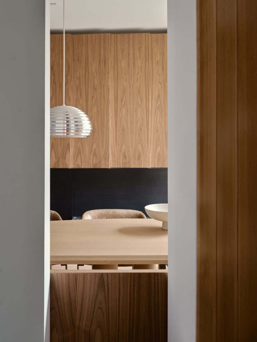 Detail minimalistického jídelního koutu s dřevěným stolem a kovovým závěsným svítidlem