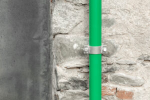 Detail jasně zeleného okapu na autentické kamenné stěně starého kurníku, kontrast materiálů a barev symbolizuje citlivé propojení původního s novým.