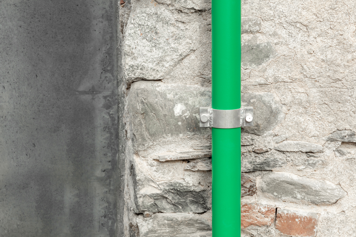 Detail jasně zeleného okapu na autentické kamenné stěně starého kurníku, kontrast materiálů a barev symbolizuje citlivé propojení původního s novým.