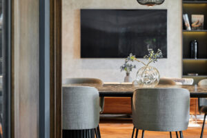 Detailní pohled na elegantní čalouněné židle v jídelně, doplněné originálními designovými svítidly z černého kovu, které tvoří výrazný kontrast k jemné kresbě dřevěné podlahy.