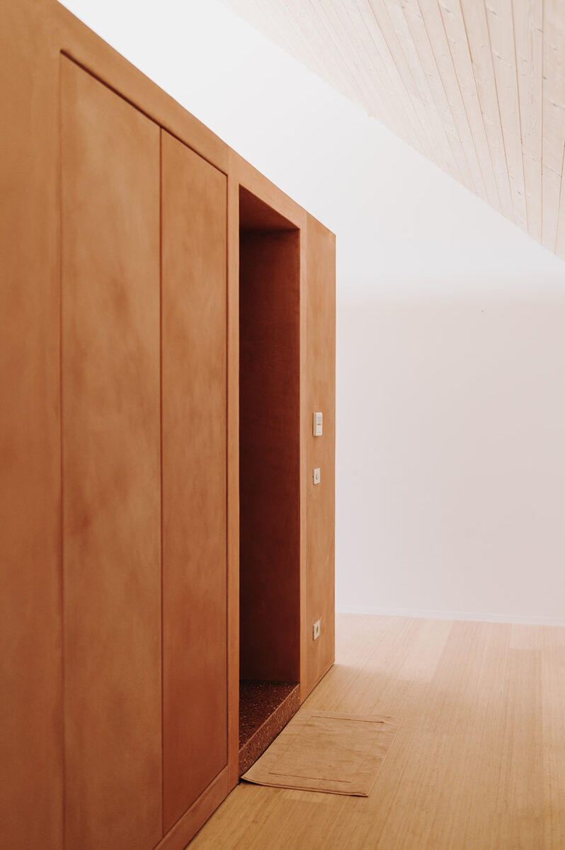 Detail minimalistické vestavěné skříně s hladkým dřevěným povrchem v podkroví.