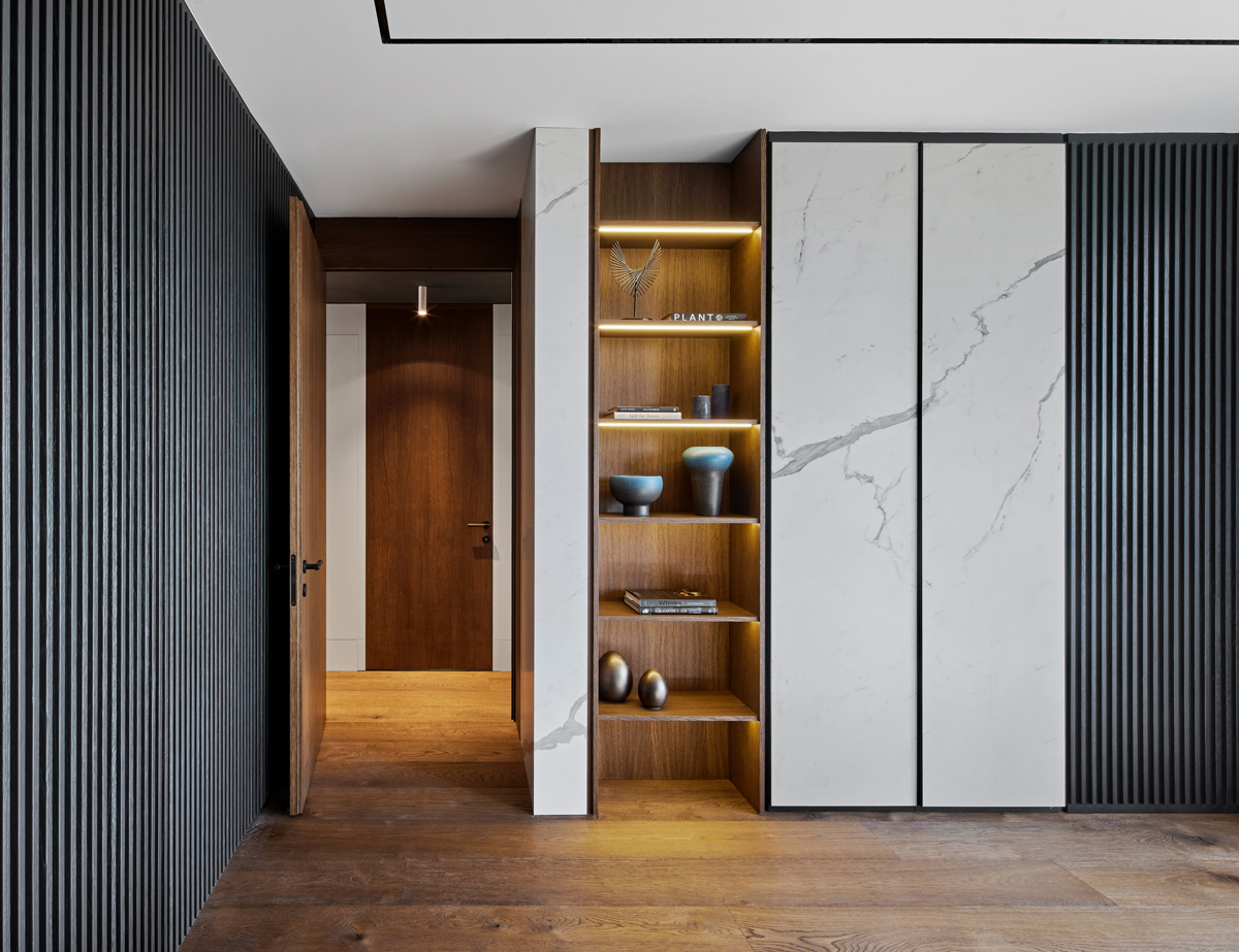 Vestavěný regál z přírodního dřeva s decentním LED podsvícením slouží nejen jako praktický úložný prostor, ale i jako stylová galerie pro designové vázy a knihy.