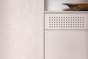 Detail růžového minimalistického nábytku a dřevěné mísy – kombinace tradičních prvků a čistého designu.