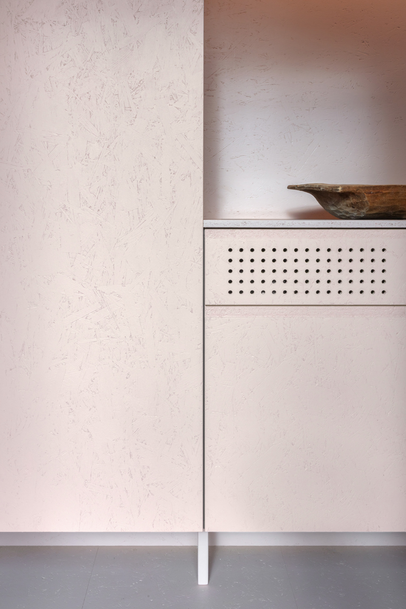 Detail růžového minimalistického nábytku a dřevěné mísy – kombinace tradičních prvků a čistého designu.