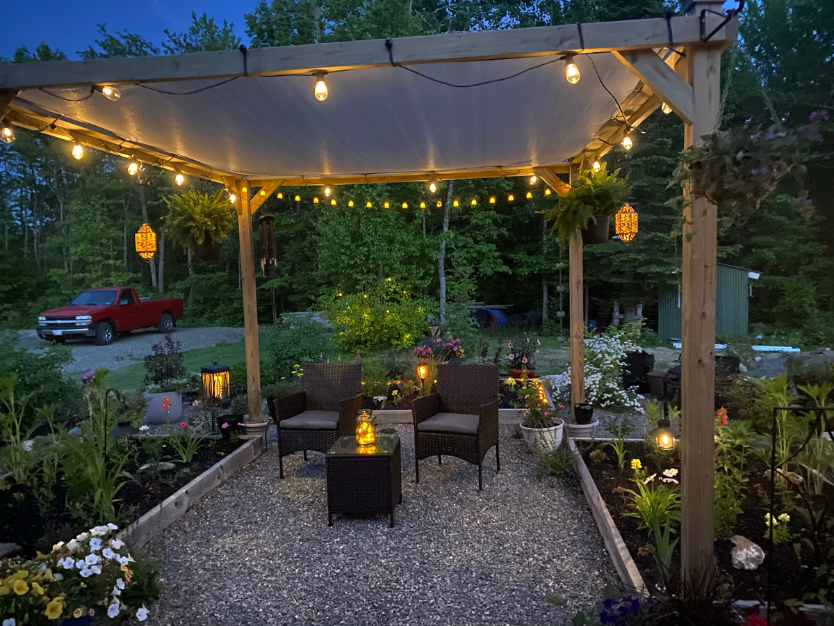 Pergola se světelným řetězem a romantickým zahradním posezením, ideální pro večerní posezení mezi květinami.