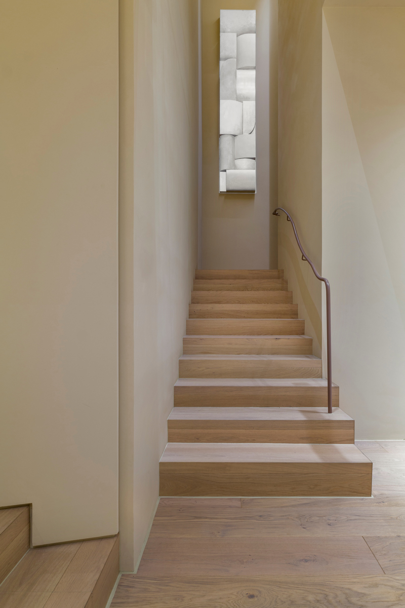 Detail minimalistického schodiště s kovovým zábradlím a uměleckou instalací.