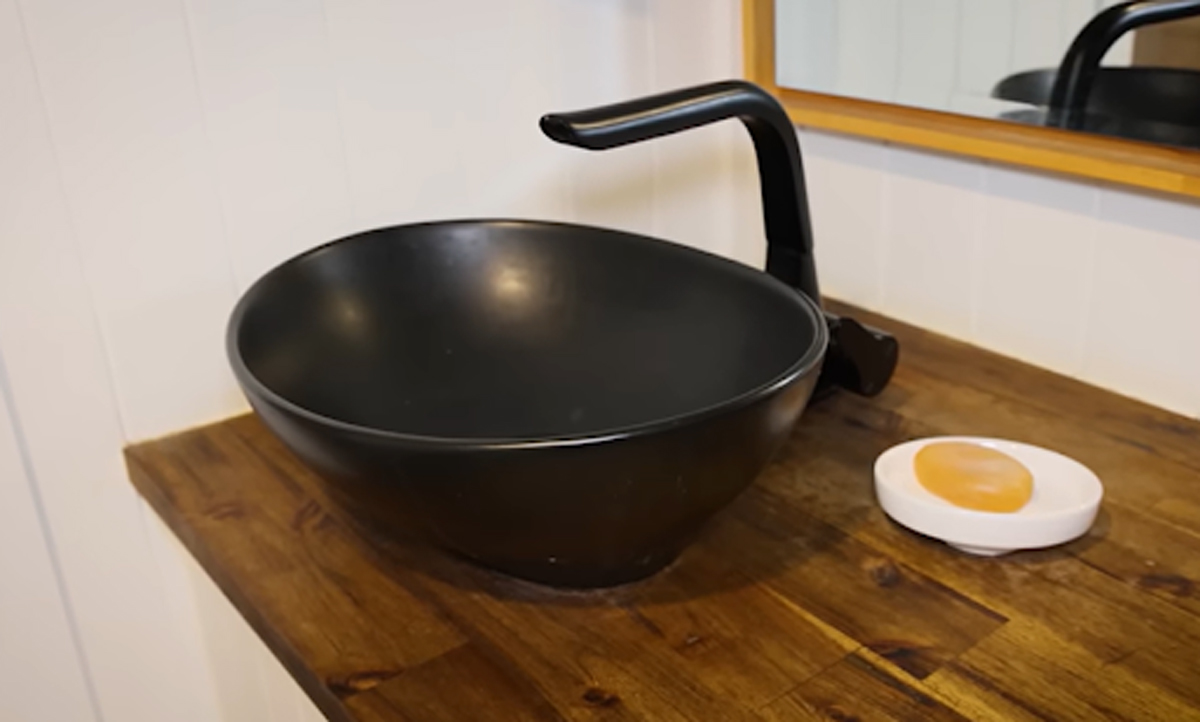 Černé umyvadlo na dřevěné desce s moderní baterií a mýdlem.