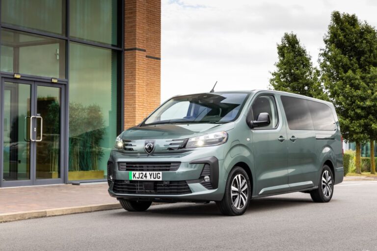 Elektrická dodávka Peugeot e-Traveller zaparkovaná před moderní administrativní budovou.