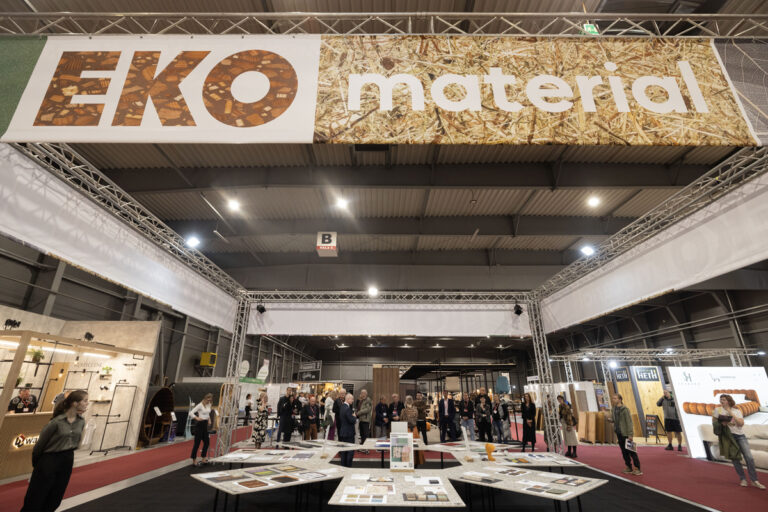 Expozice „EKO materiál“ na veletrhu – velký banner v hale, stoly se vzorky a skupiny návštěvníků v zóně.