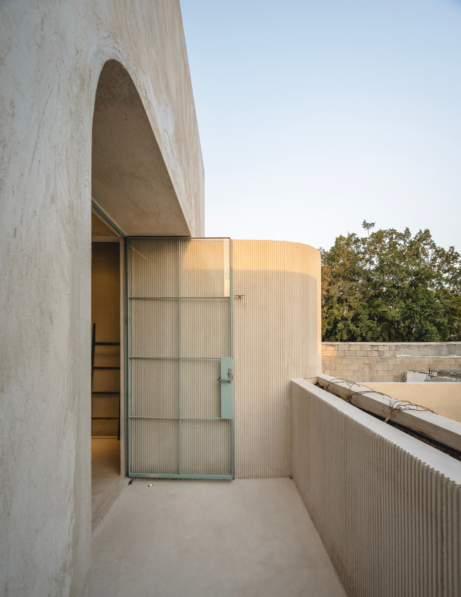 Minimalistický balkon s betonovým zábradlím a prosklenými dveřmi do ložnice.