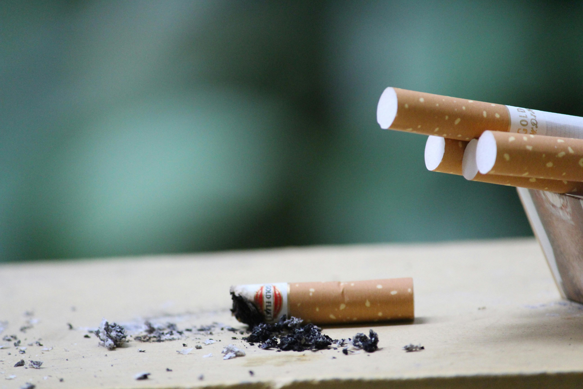 Ohořelý nedopalek a rozptýlený popel vedle krabičky s několika cigaretami.