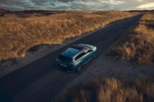 Peugeot 308 SW jede opuštěnou silnicí mezi písečnými dunami při zapadajícím slunci, pohled shora.
