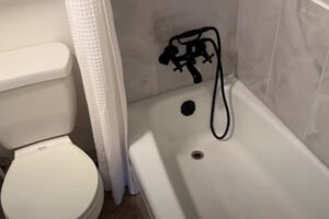 Malá koupelna s WC a vanou, černá baterie se sprchovou hadicí a bílý texturovaný závěs.